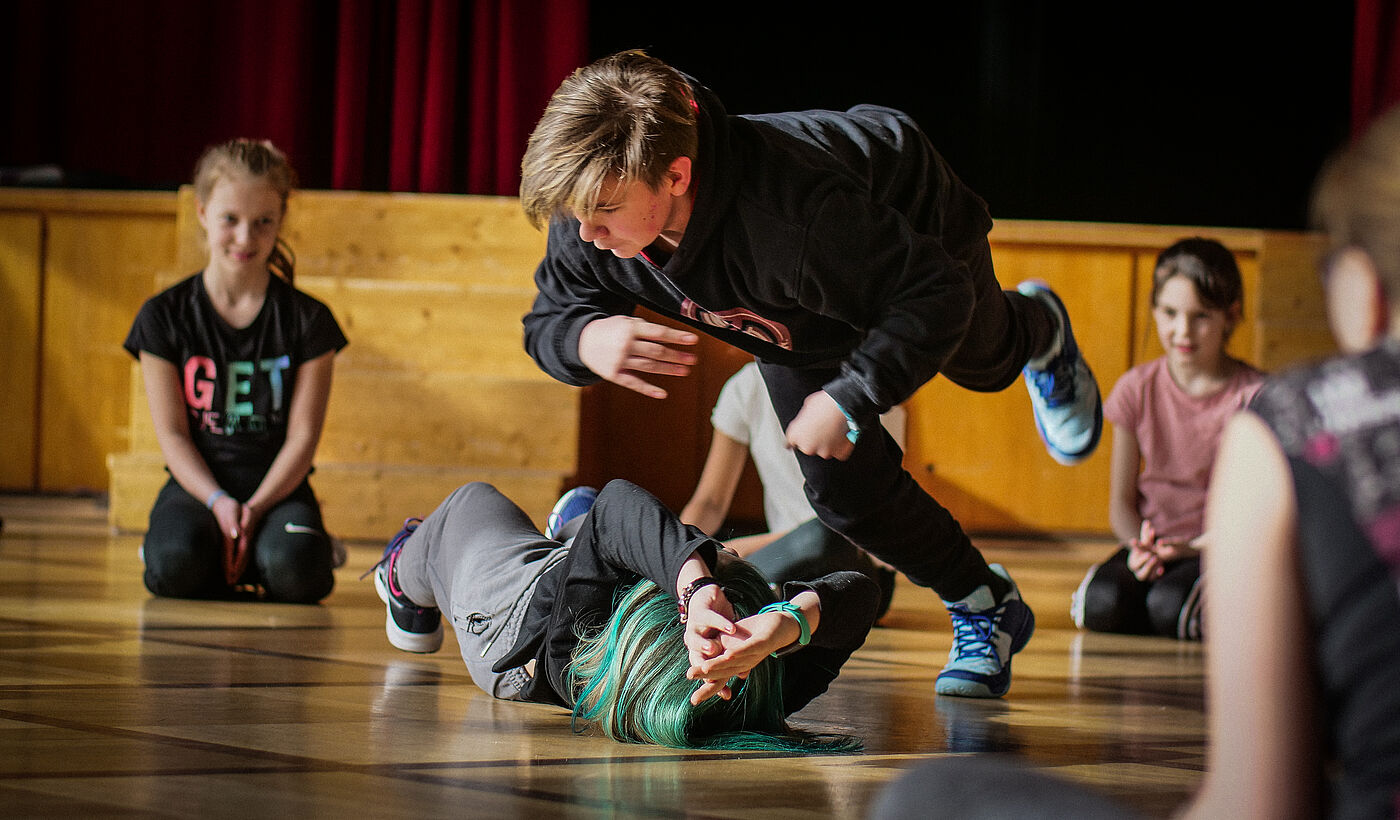 Kinder machen Breakdance Bewegungen auf einer Bühne.