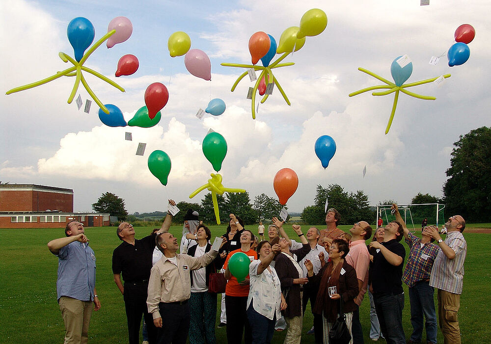 Eine Gruppe Lehrerinnen und Lehrer lassen auf einem Fußballfeld Ballons steigen.